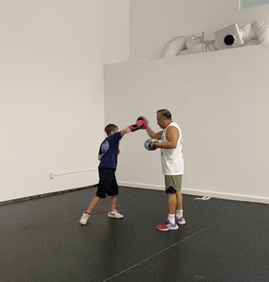 Coach holding pads for a young boxer during a kids class